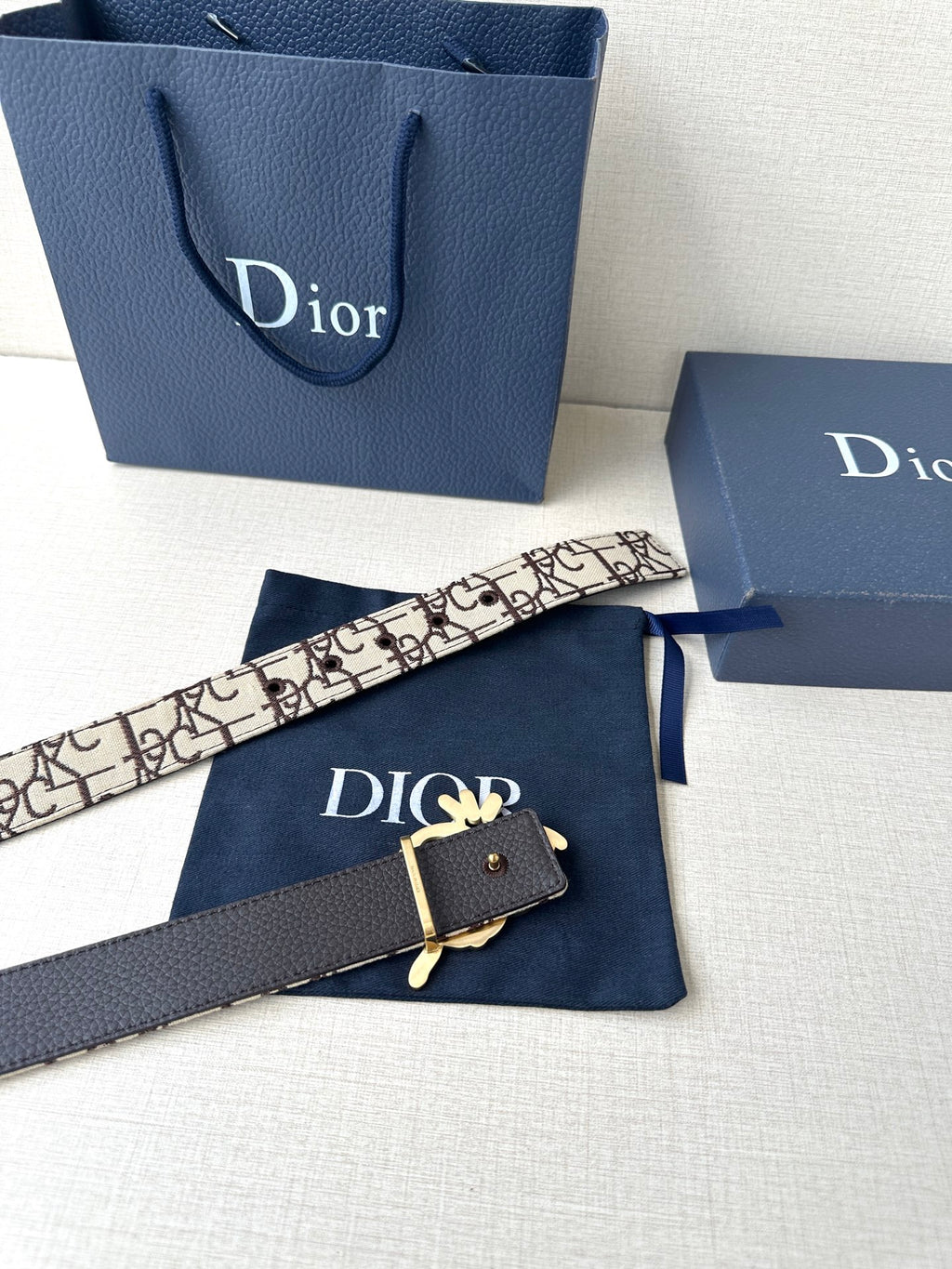 Dior belt with beige logo strap, black underside, and gold-toned emblem clasp