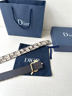 Dior belt with beige logo strap, black underside, and gold-toned emblem clasp