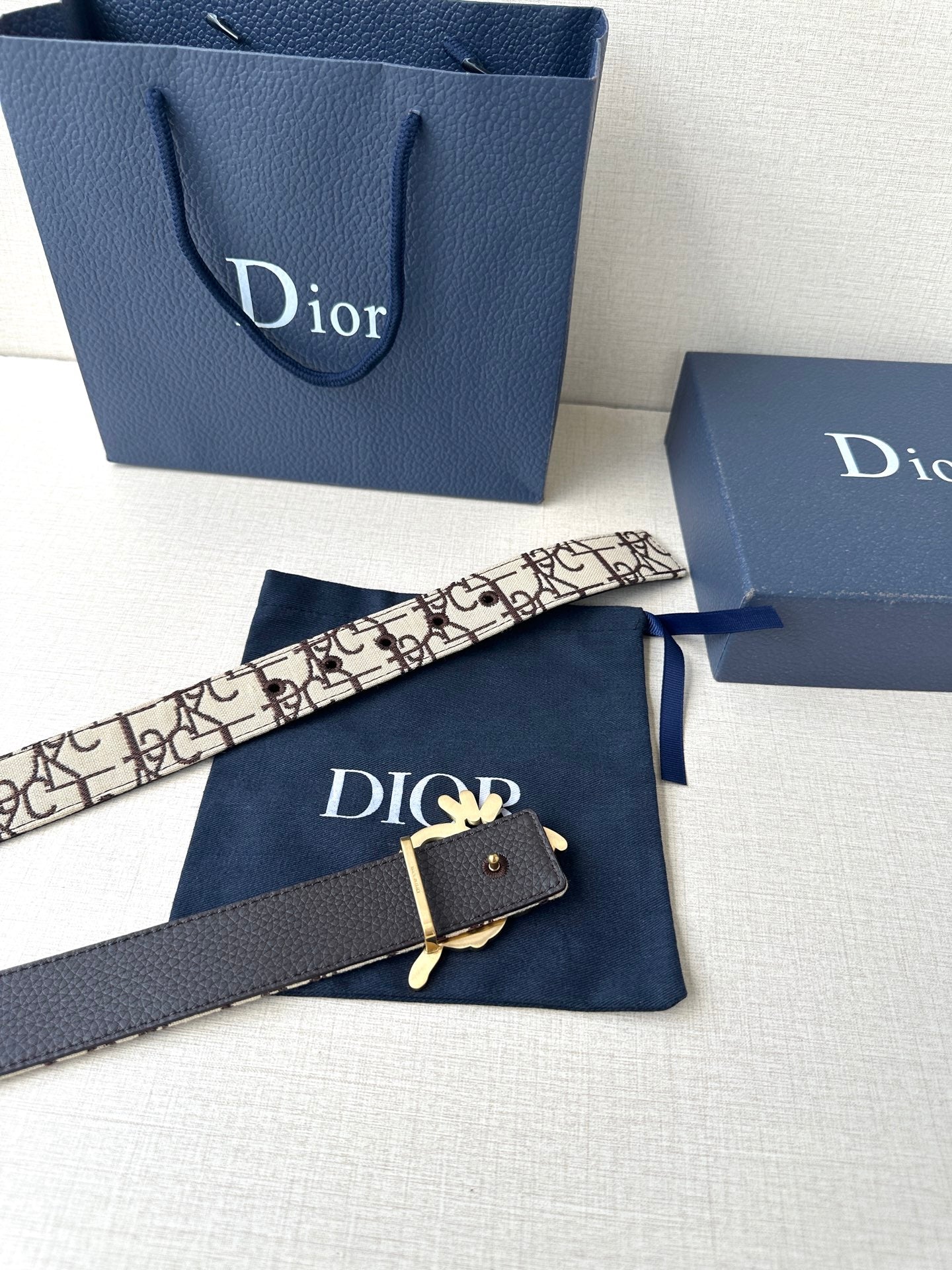 Dior belt with beige logo strap, black underside, and gold-toned emblem clasp