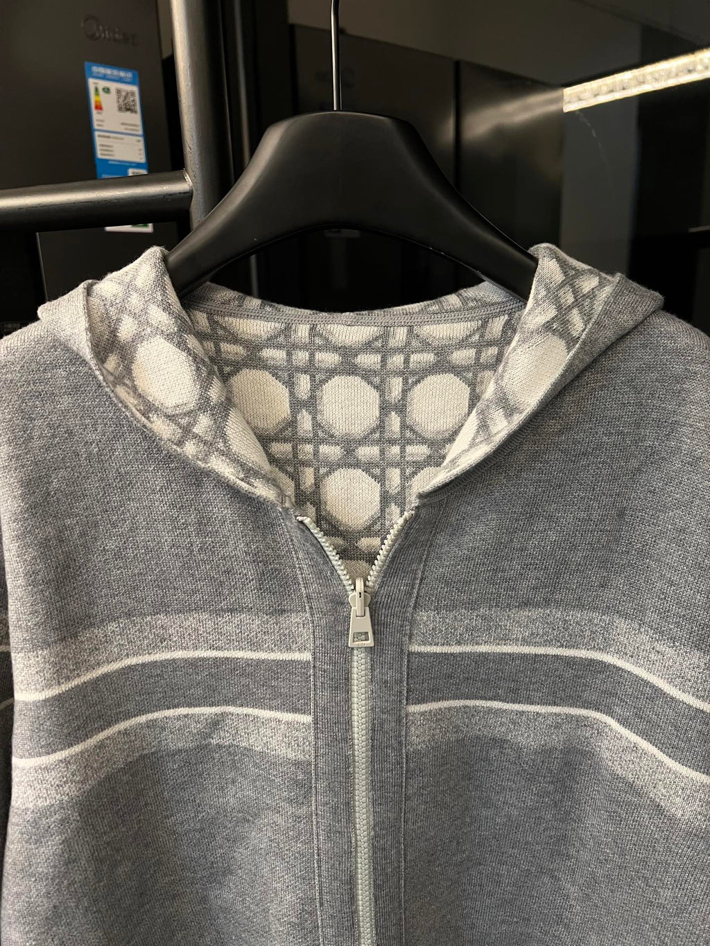 Grey zip-up hoodie close-up with white monogram pattern hood and front zipper
