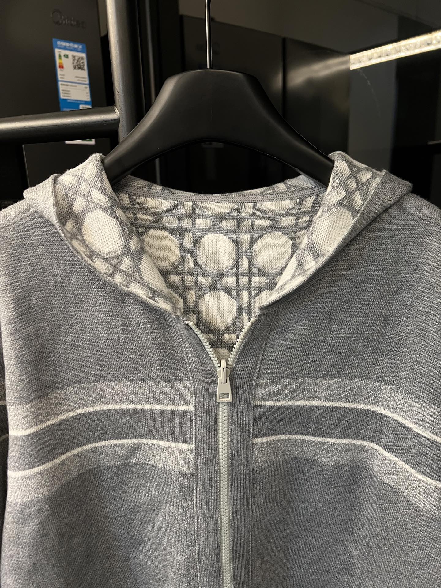 Grey zip-up hoodie close-up with white monogram pattern hood and front zipper