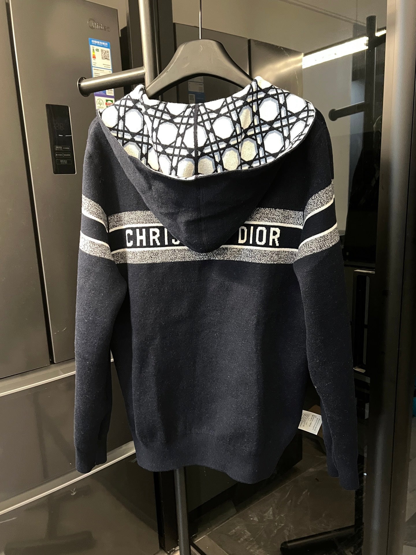 Dark hooded zip-up jacket with lattice-lined hood and white stripe bands at shoulders
