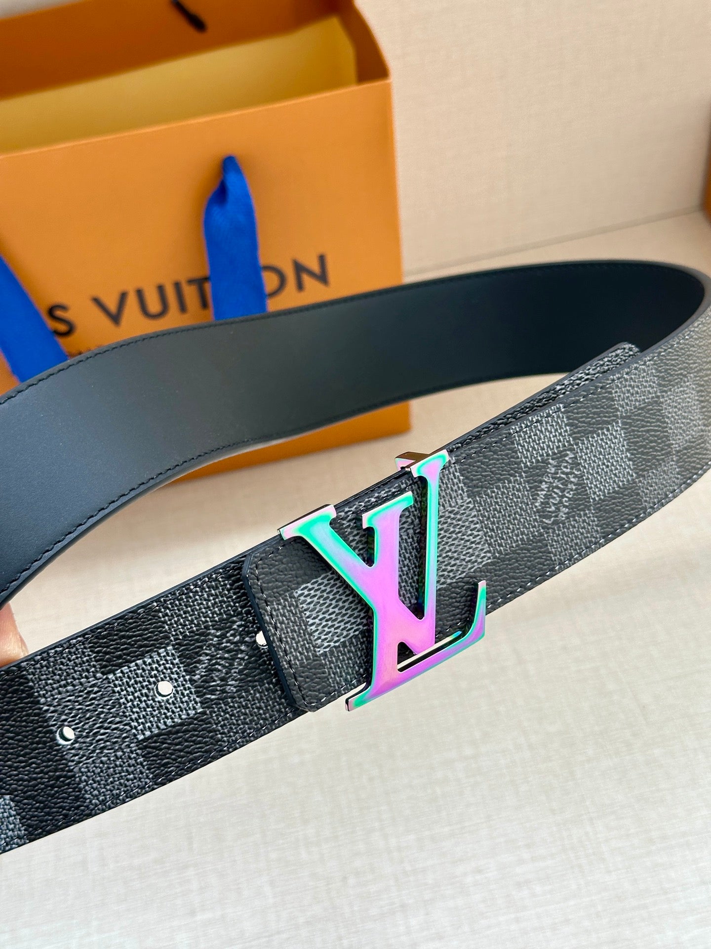 Gray checkered belt close-up with multicolor LV buckle and belt holes