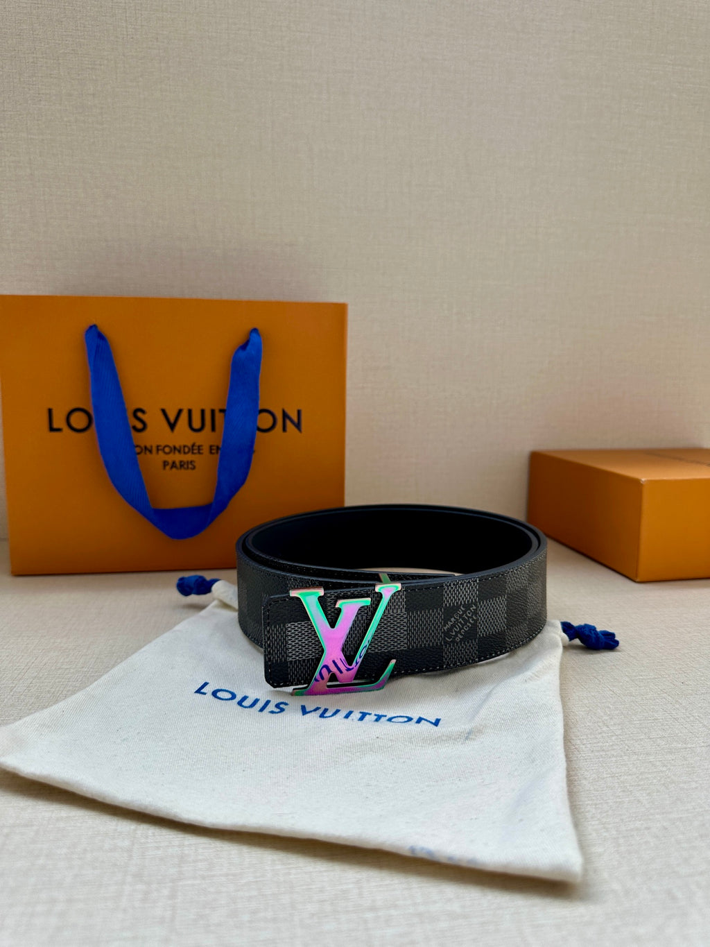 Gray checkered belt with multicolor LV buckle resting on fabric pouch