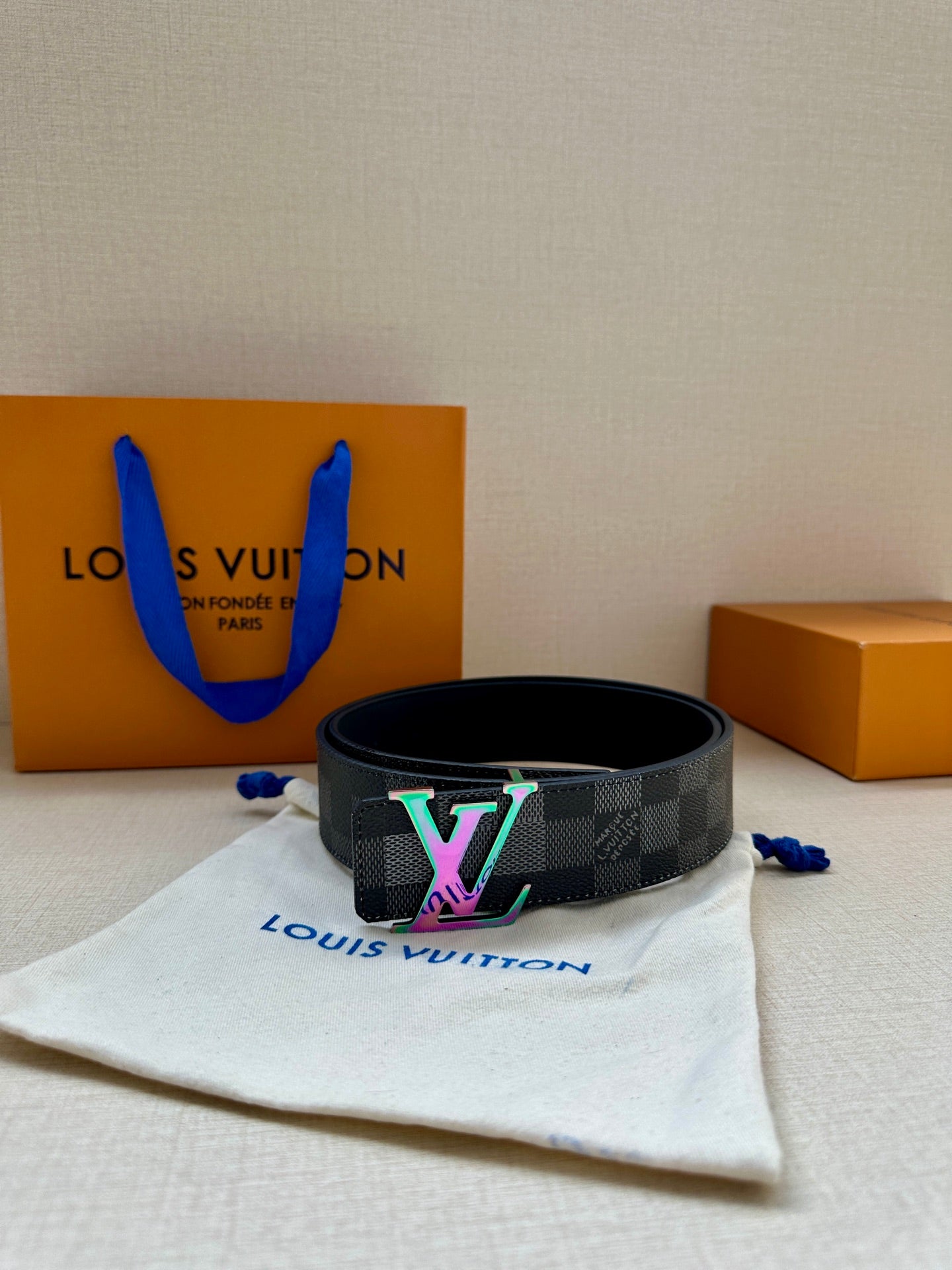 Gray checkered belt with multicolor LV buckle resting on fabric pouch