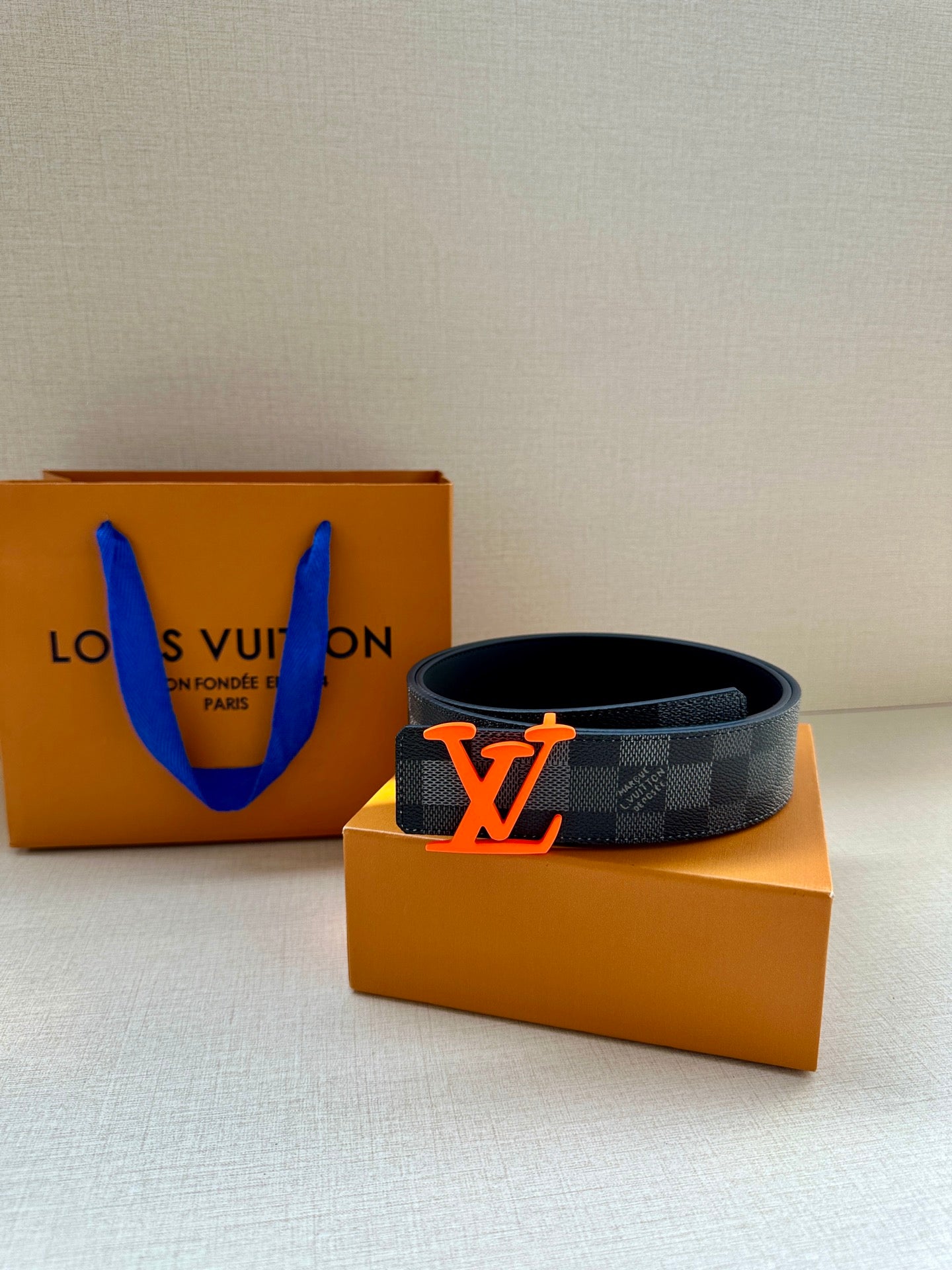 Louis Vuitton belt on orange shopping boxes, featuring dark check pattern and LV buckle