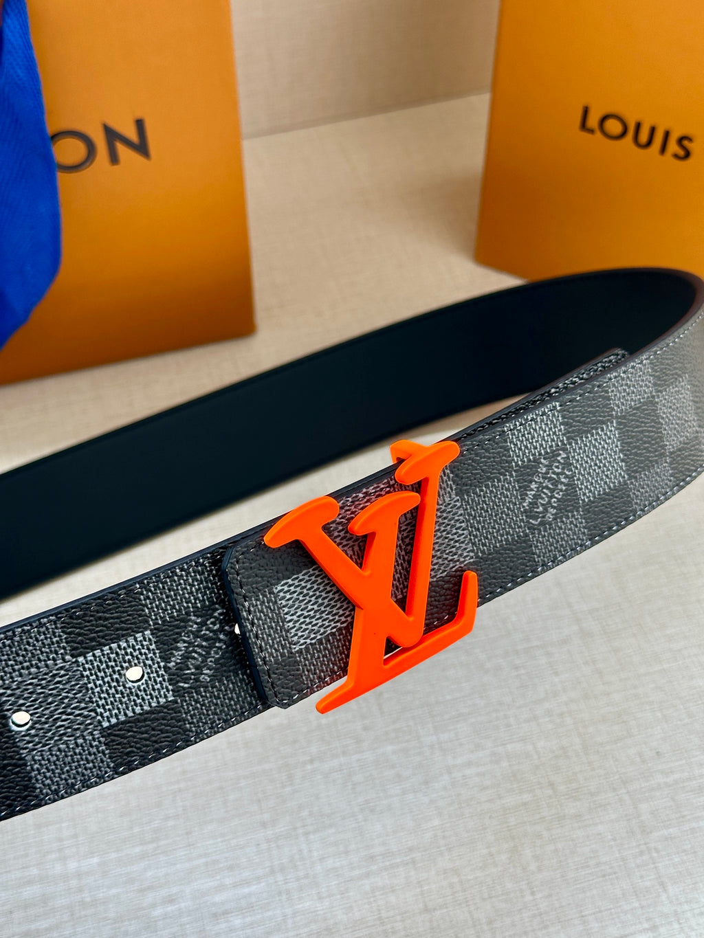 Louis Vuitton belt close-up with dark check pattern and orange LV buckle
