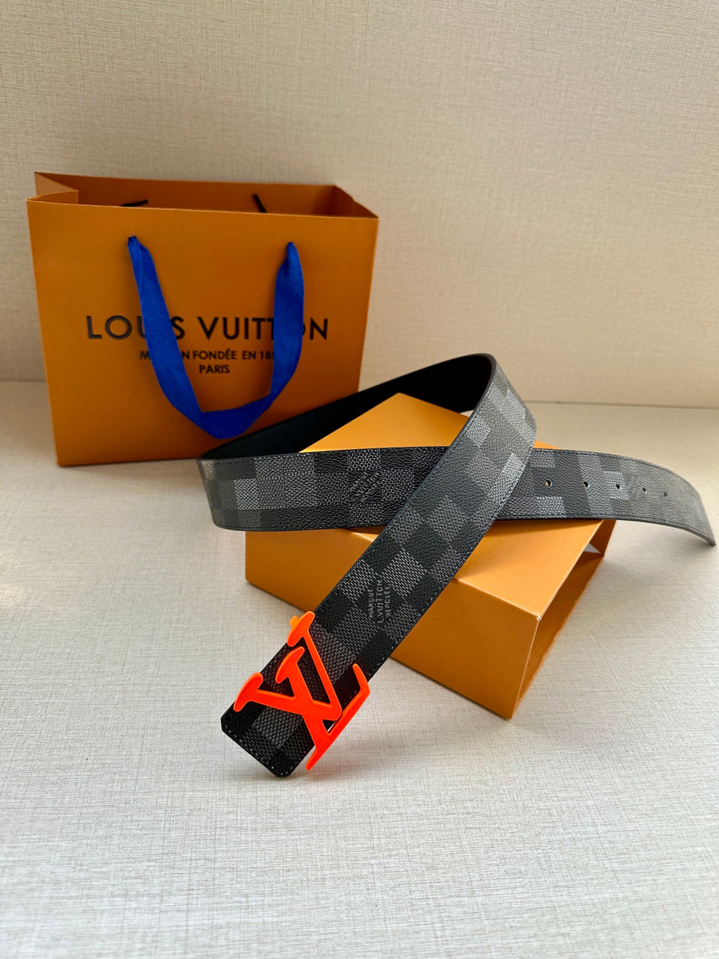 Louis Vuitton belt with dark check pattern draped over orange boxes and bag
