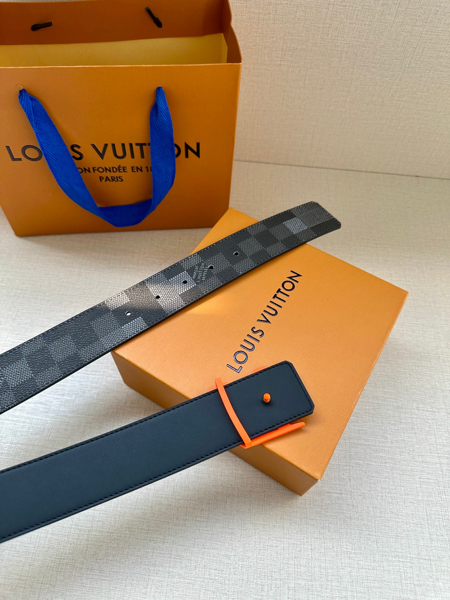 Louis Vuitton belt with dark check pattern on box with orange card and orange buckle