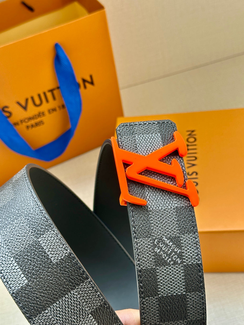 Louis Vuitton belt close-up on orange box, showing orange LV buckle and textured strap