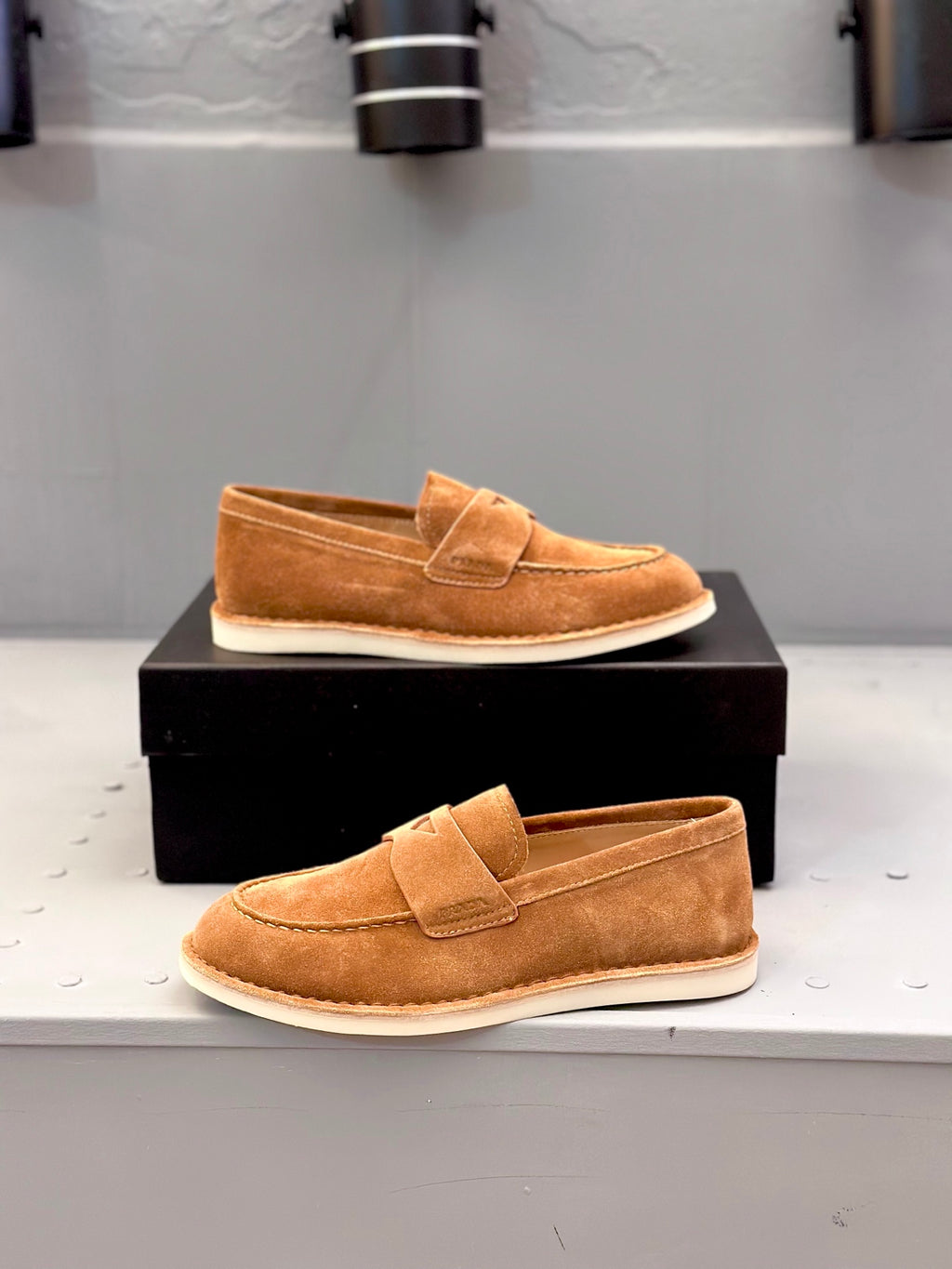 Tan suede loafers on black box, slip-on design with top strap