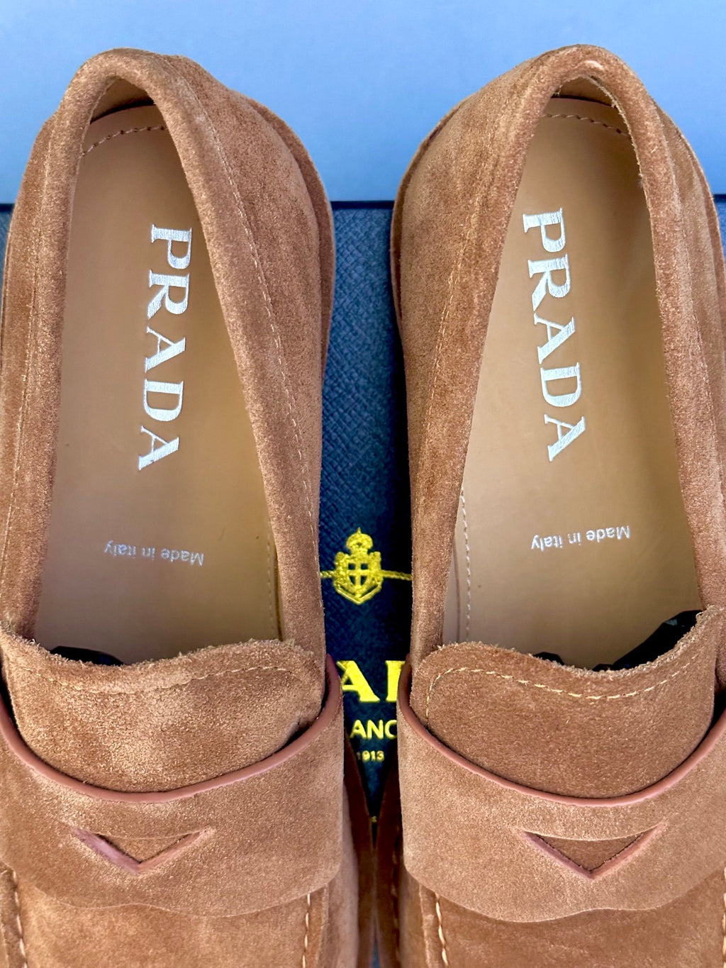Close-up of tan suede loafers showing Prada logo on interior lining