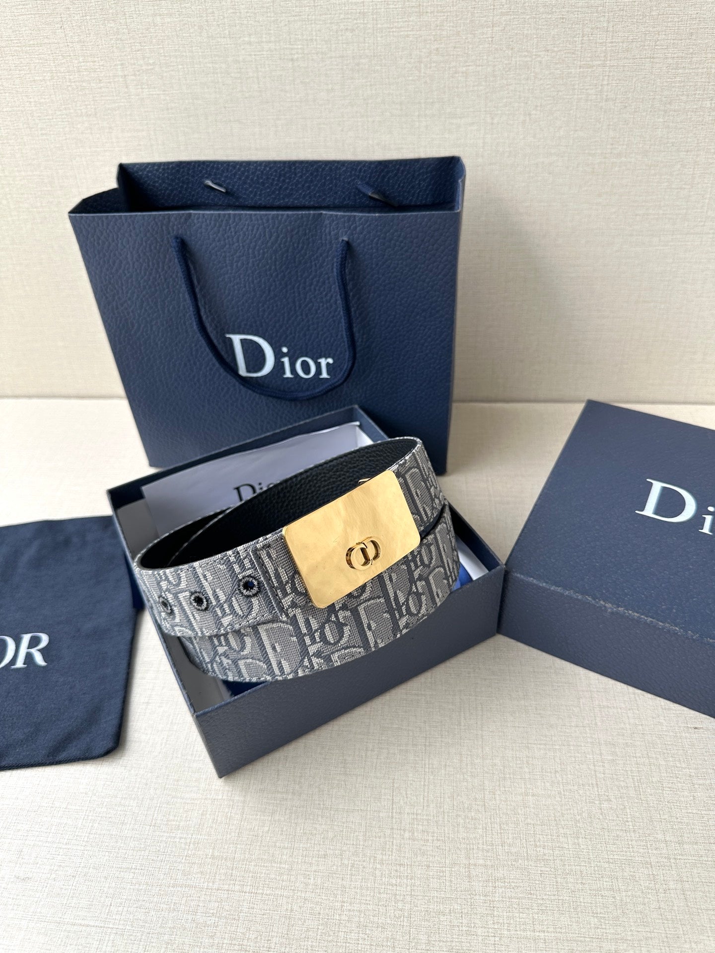 Dior belt with gray patterned strap and gold-tone buckle, shown with gift packaging