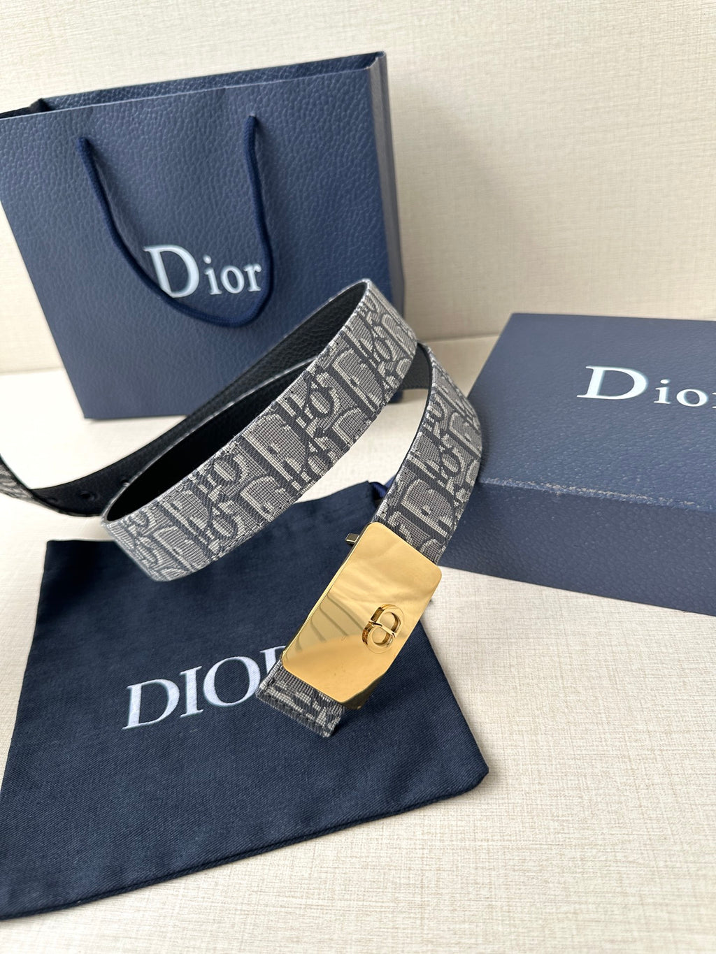 Dior belt on navy box: gray monogram strap with gold buckle and black lining