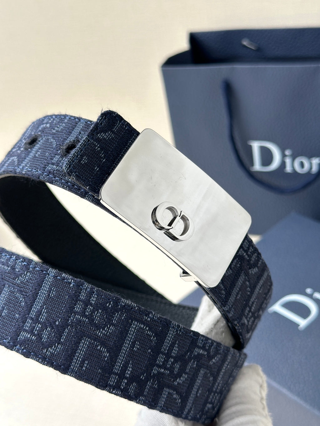 Dior belt close-up: navy patterned strap with silver buckle and visible strap stitching.