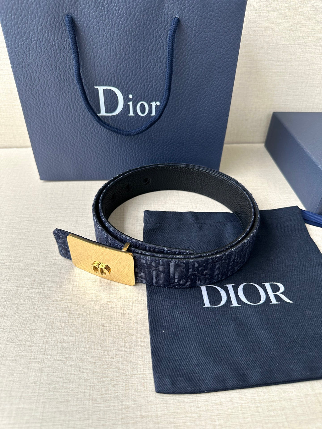Dior belt with navy patterned strap and gold-tone buckle plaque, strap end with holes.