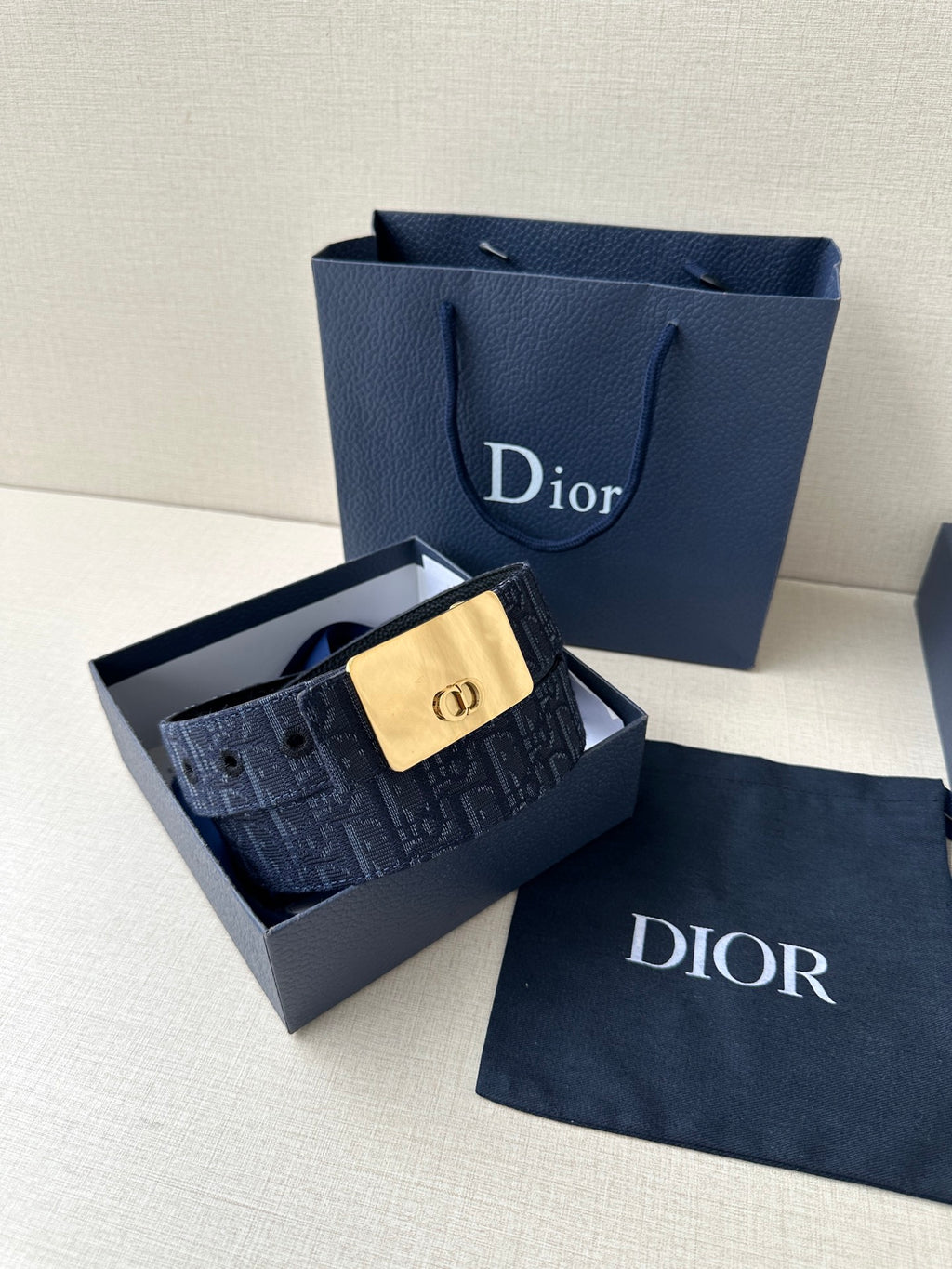Dior belt in open box: navy patterned strap with gold-tone buckle plaque and strap holes.