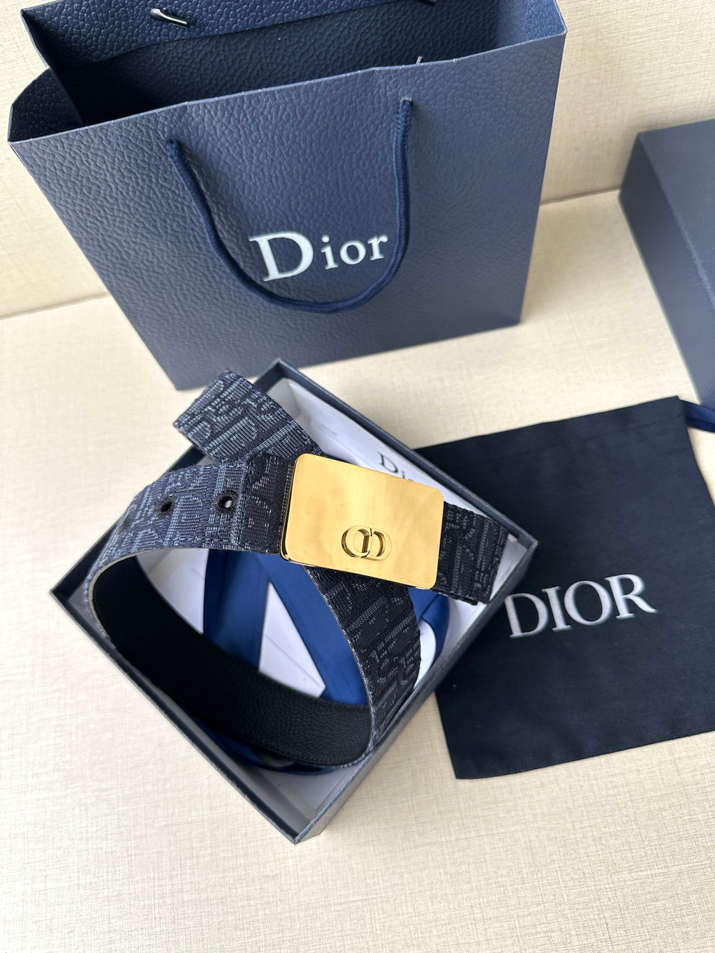 Dior belt shown with navy patterned strap and gold-tone buckle plaque, laid in box.