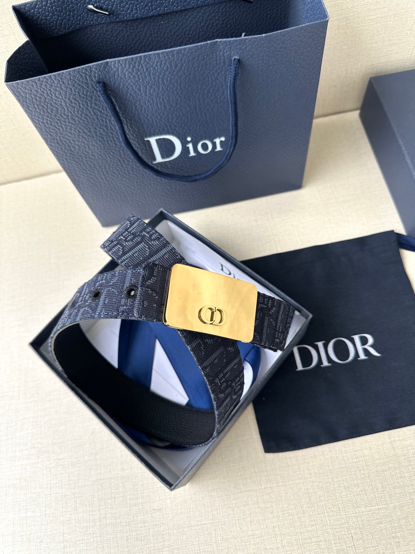Dior belt shown with navy patterned strap and gold-tone buckle plaque, laid in box.