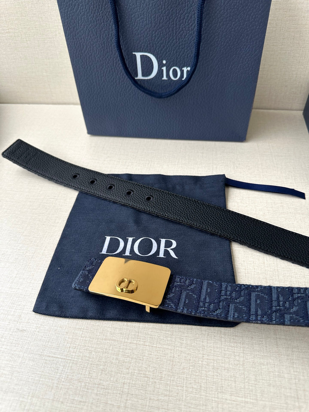 Dior belt on dust bag: navy patterned strap with gold-tone buckle and extended strap end.