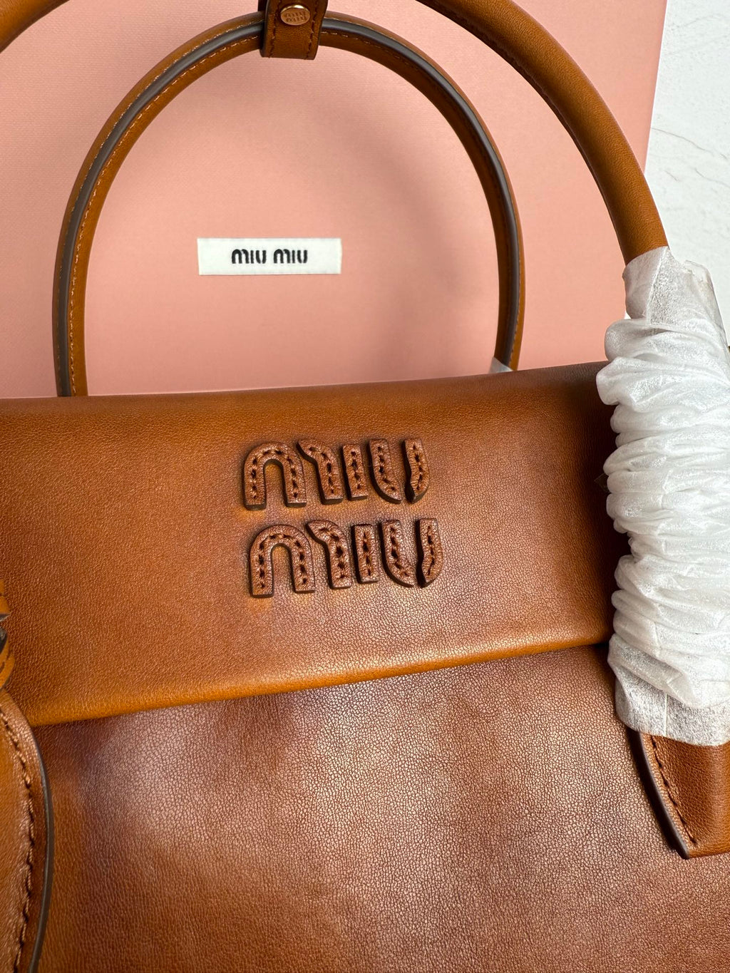 Brown MiuMiu bag front flap with embossed logo and top handle opening