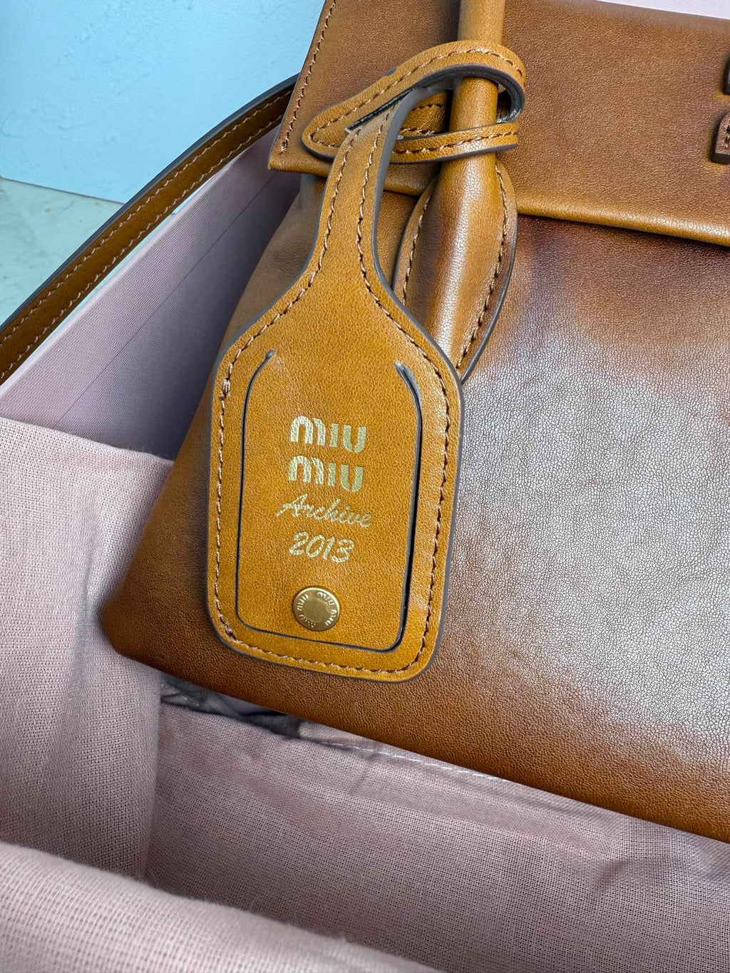 Brown leather MiuMiu bag charm with logo patch and “Archive 2013” text