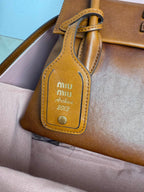 Brown leather MiuMiu bag charm with logo patch and “Archive 2013” text