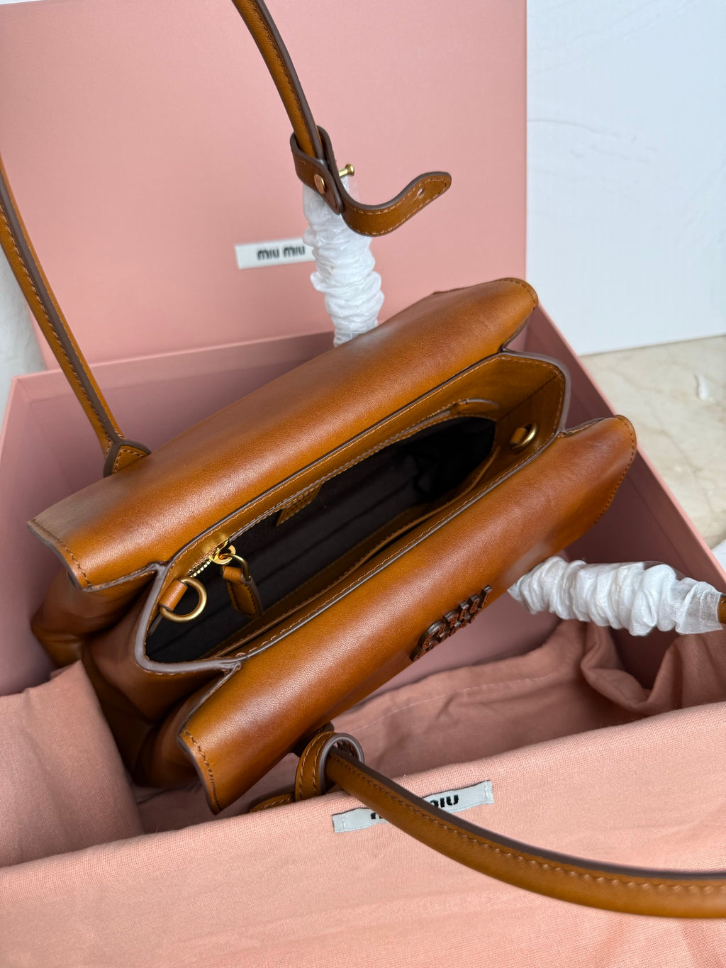 Brown MiuMiu bag with open flap, dark lining, and gold zipper pull