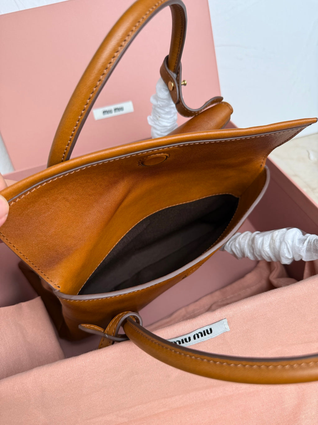 Brown MiuMiu bag with open top, dark interior, and leather shoulder strap
