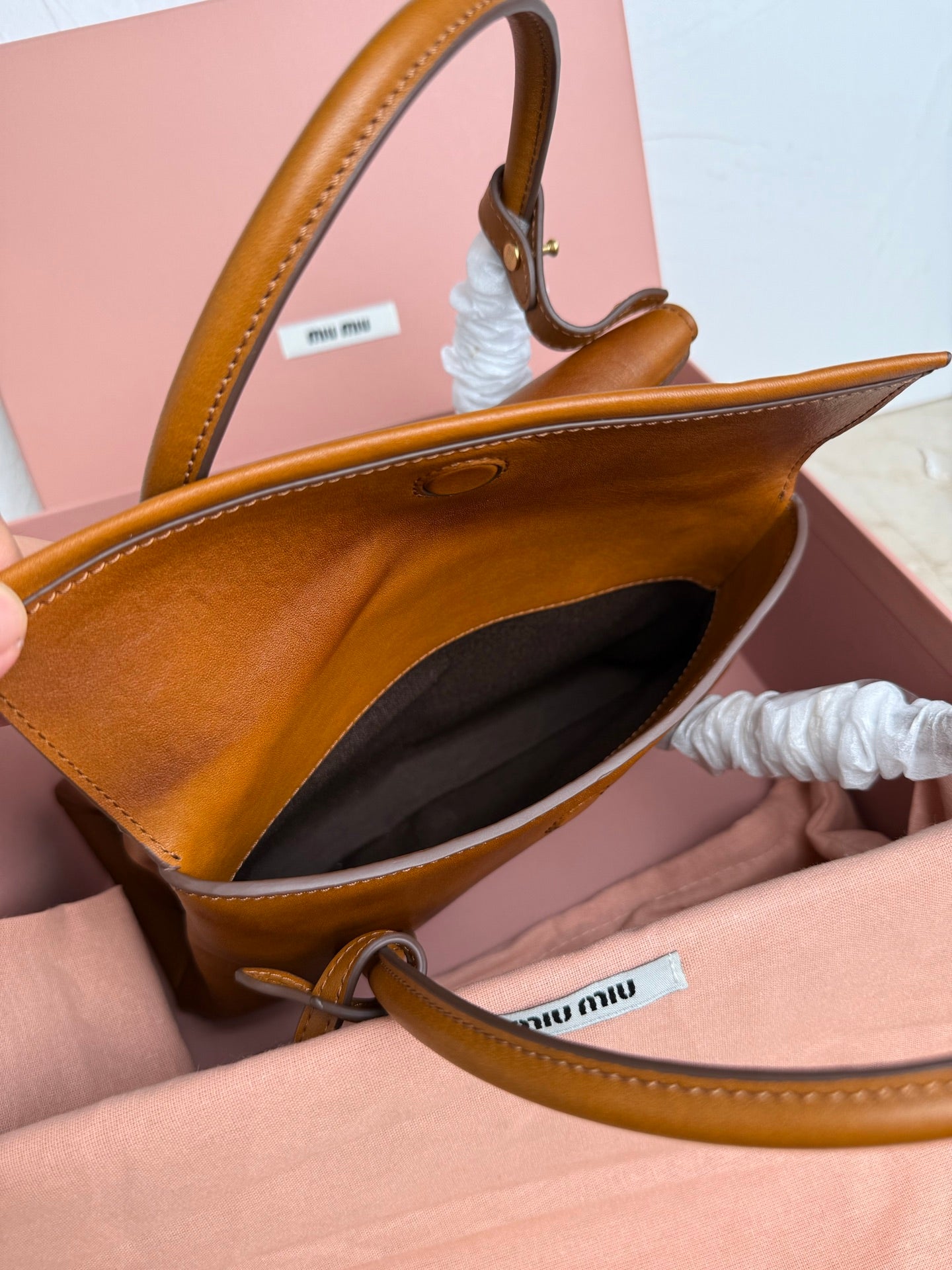 Brown MiuMiu bag with open top, dark interior, and leather shoulder strap