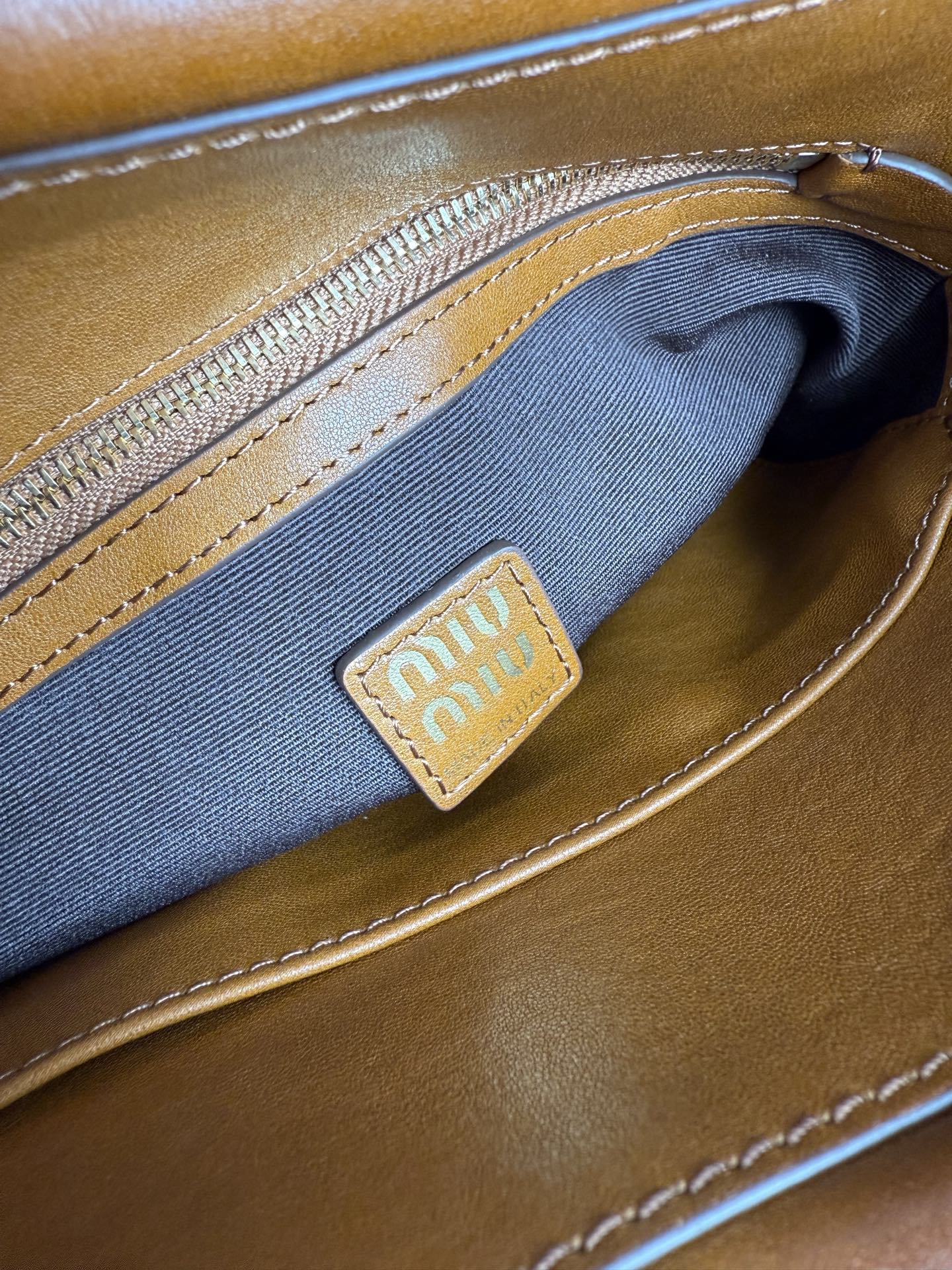 Brown MiuMiu bag interior pocket with blue fabric lining and logo patch
