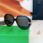 Sunglasses with black frames, dark green lenses, and gold bridge detail