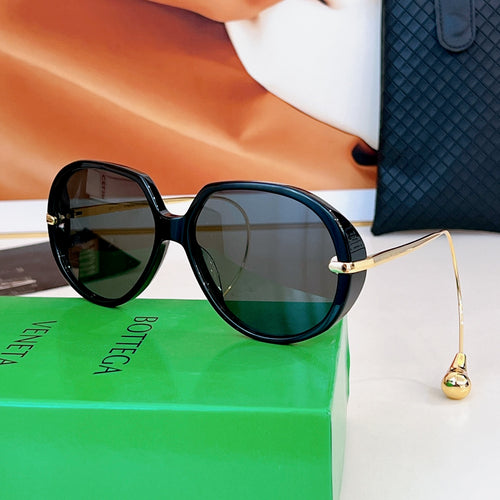 Sunglasses with black frames, dark green lenses, and gold bridge detail