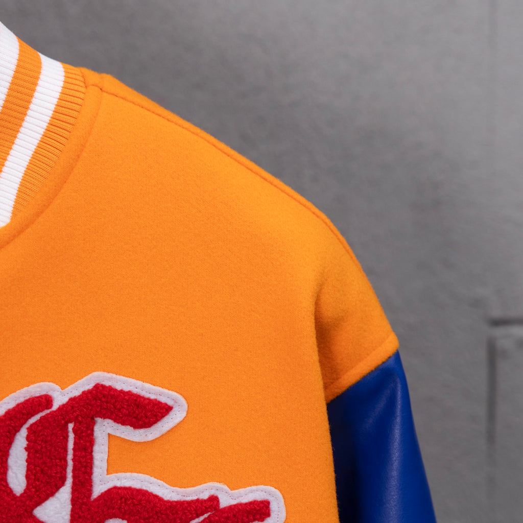 Orange varsity jacket shoulder close-up with blue sleeve panel and partial patch