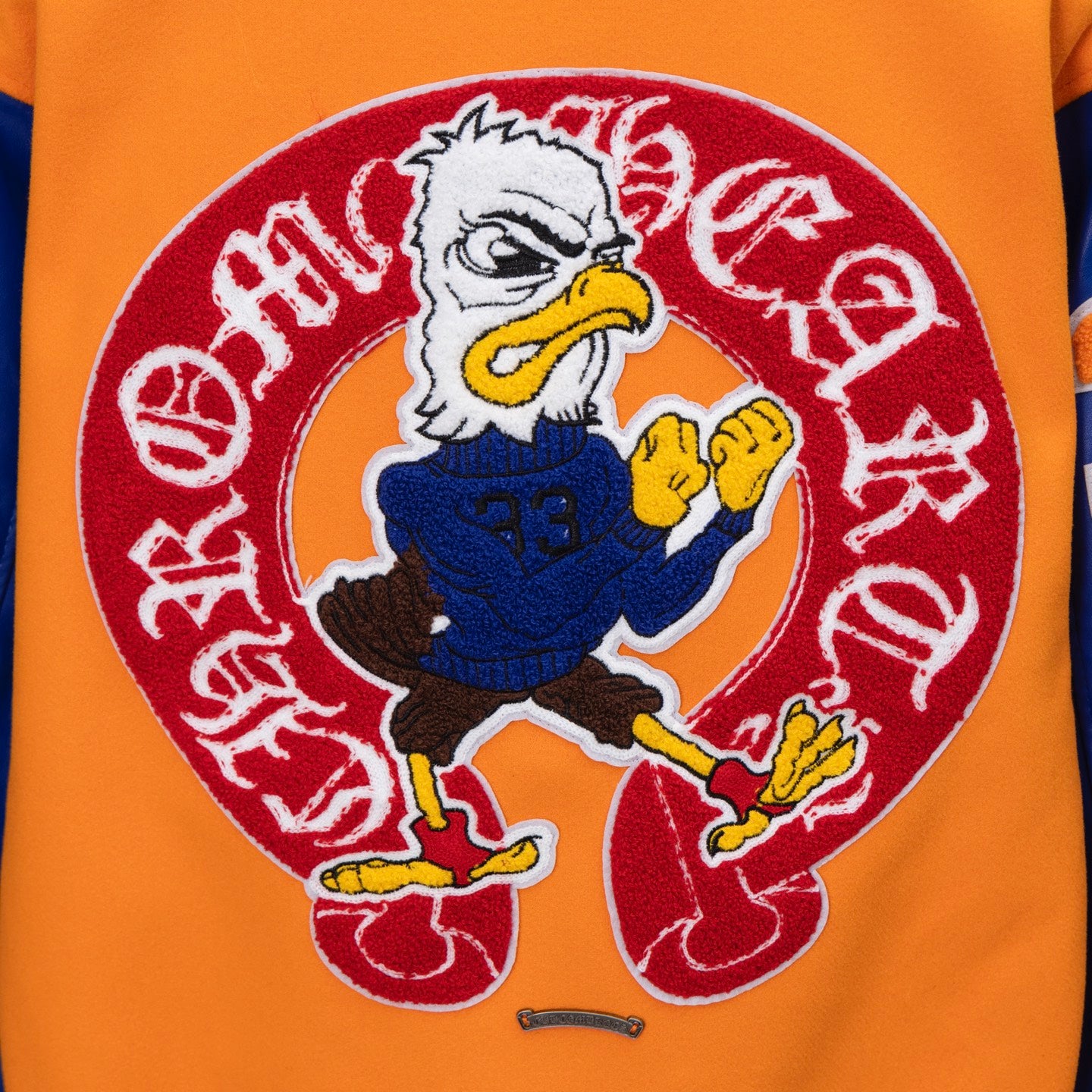 Orange varsity jacket chest graphic featuring a cartoon character in red emblem