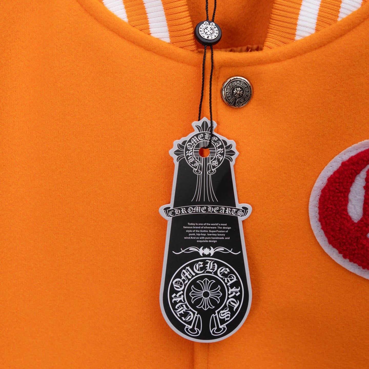 Orange varsity jacket neck close-up with hanging hangtag and round metal button