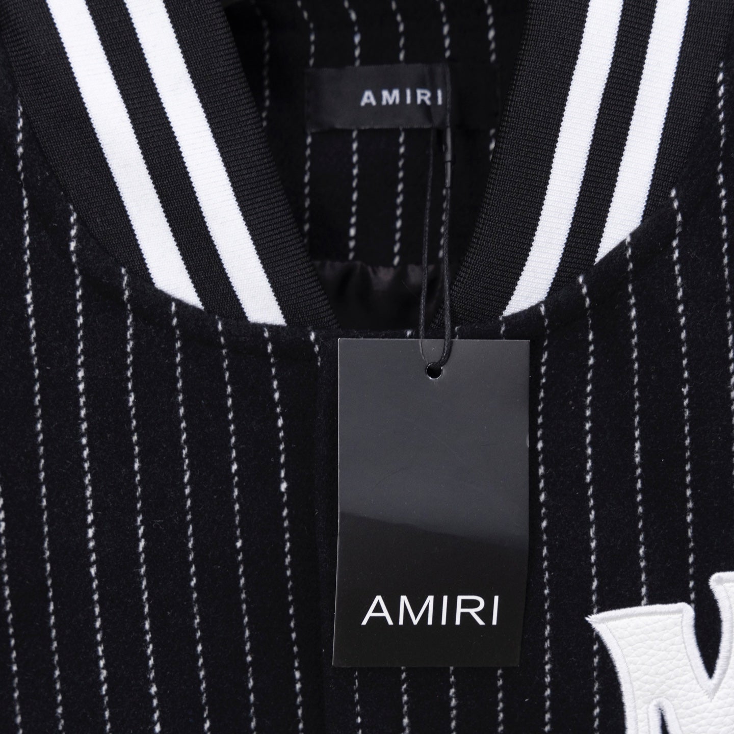 AMIRI logo patch detail on pinstripe varsity jacket, with hanging tag