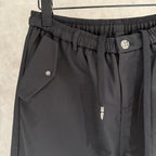 Black pants close-up of elastic waistband, side pocket flap, and small logo button.