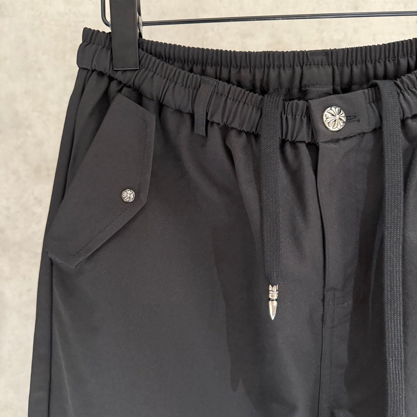 Black pants close-up of elastic waistband, side pocket flap, and small logo button.
