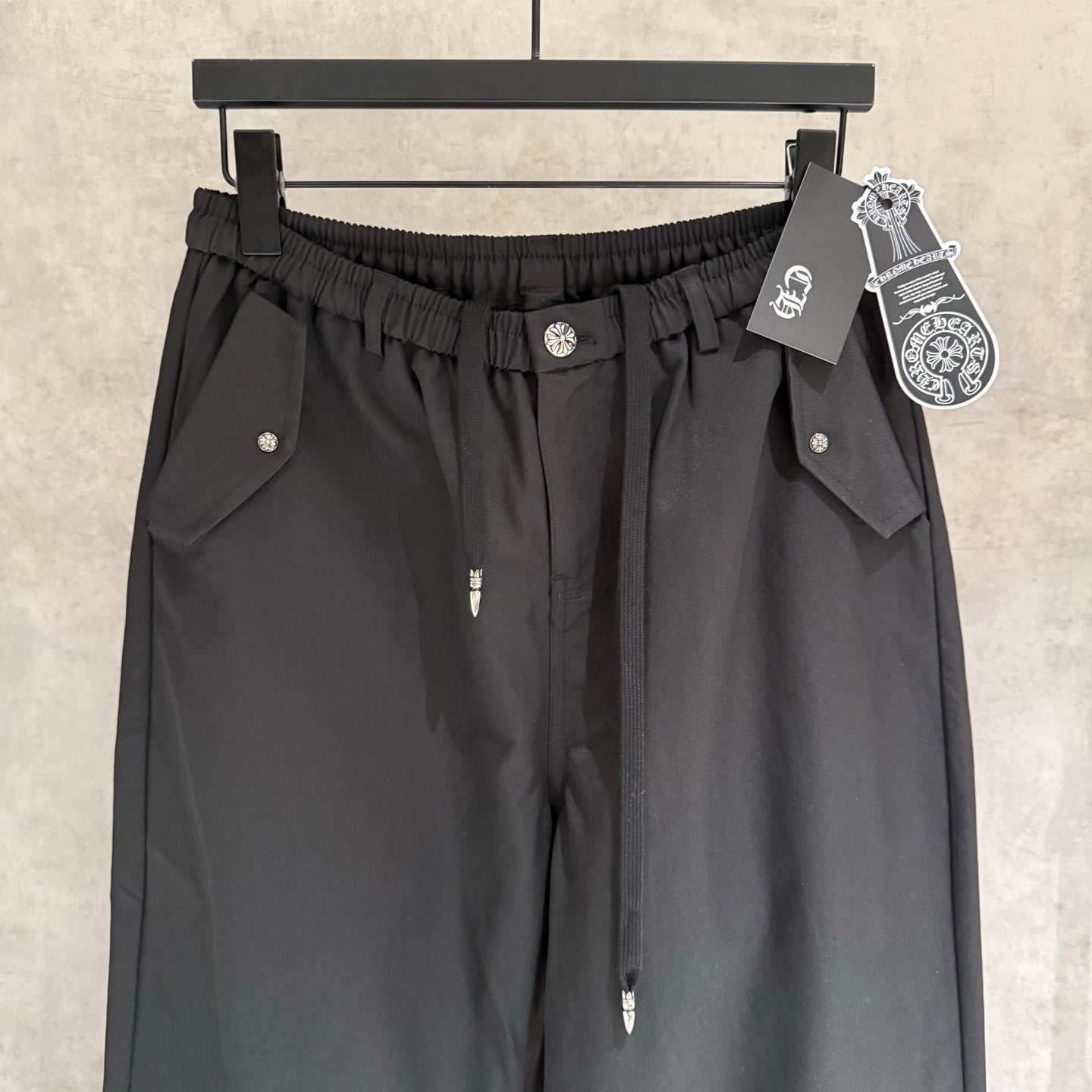 Black elastic-waist pants with two front flap pockets and small chest-like logo detail.