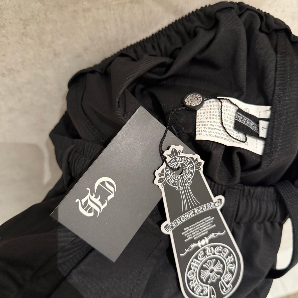 Black pants waistband with hang tags attached; elastic top edge visible.