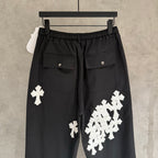 Black wide-leg pants with elastic waistband, flap pockets, and white cross appliques.