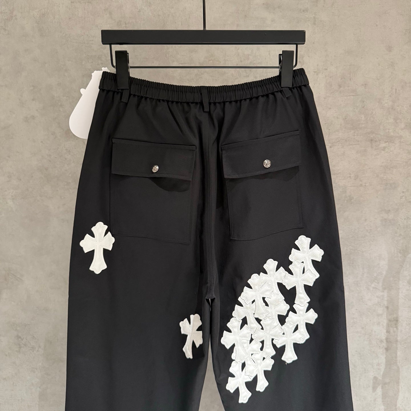 Black wide-leg pants with elastic waistband, flap pockets, and white cross appliques.