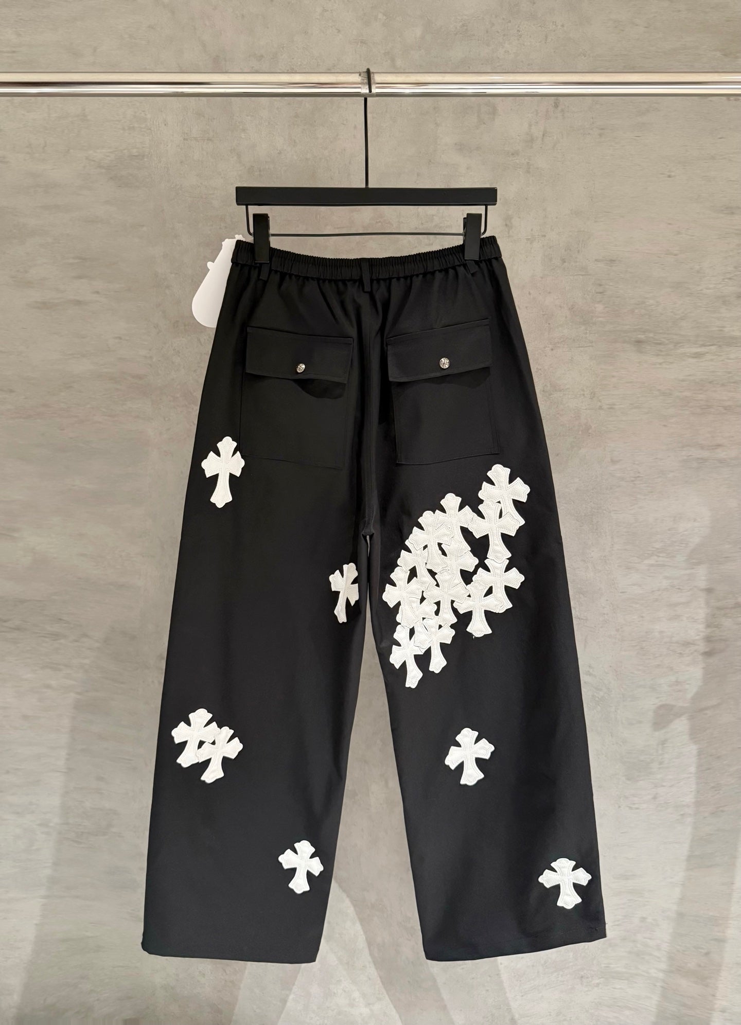 Black wide-leg pants with elastic waistband and white cross-shaped appliques.