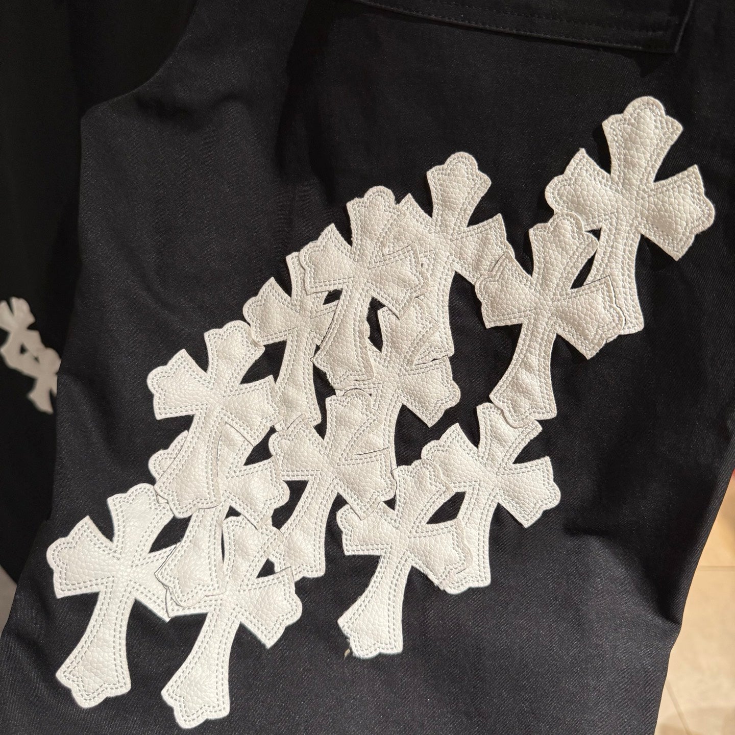 Black pants with large white cross applique graphic on the front leg.