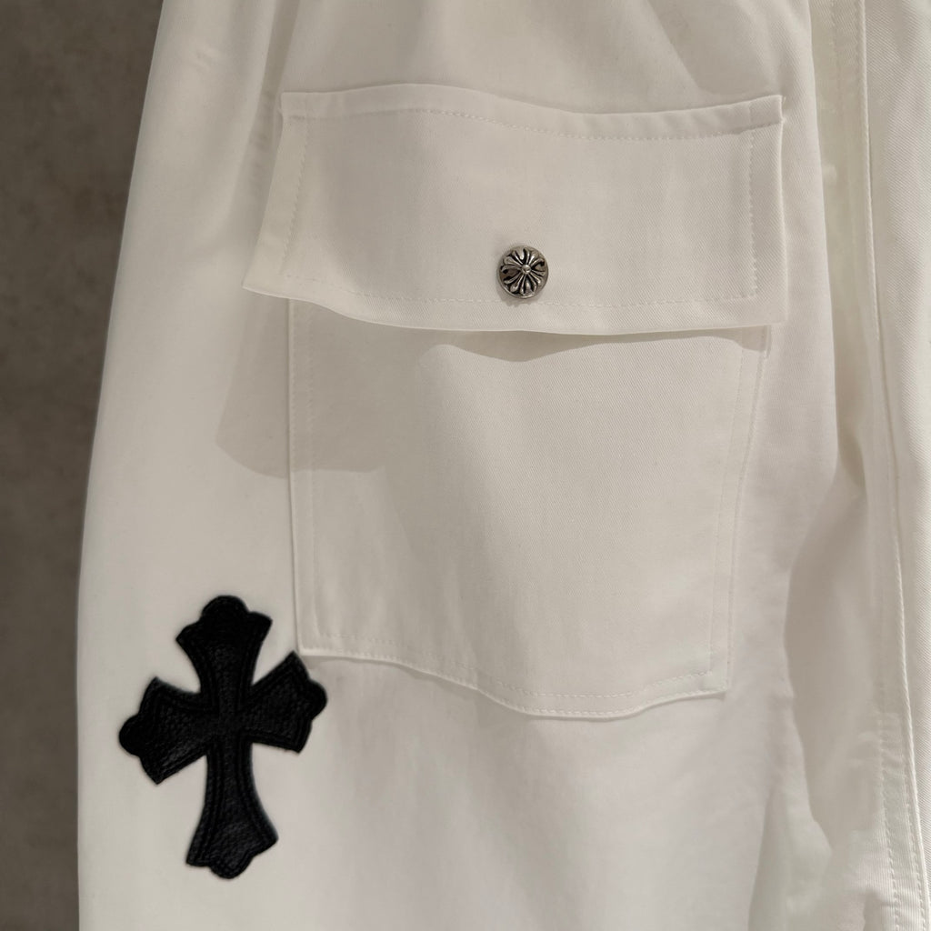White pants with buttoned flap pocket and black cross applique