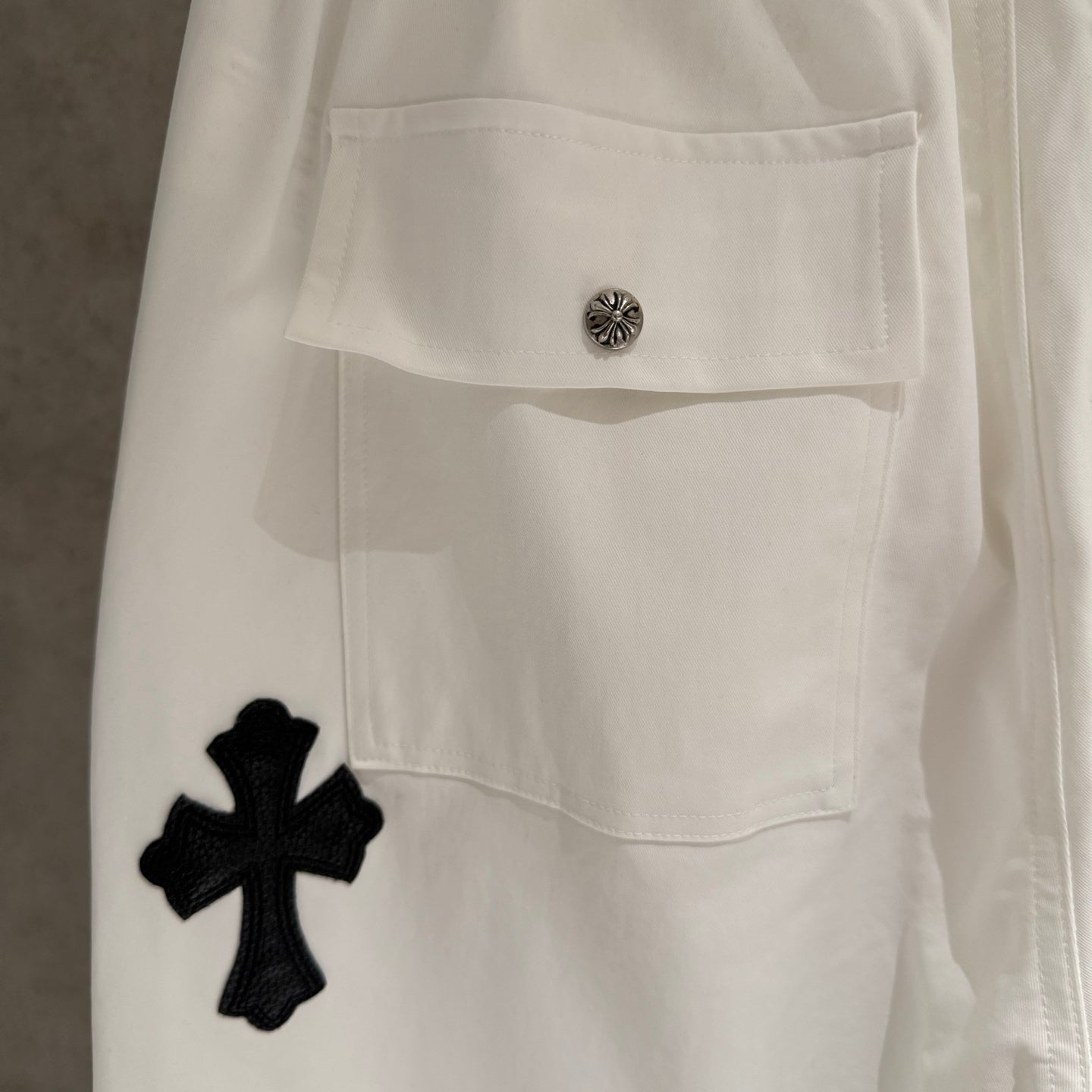 White pants with buttoned flap pocket and black cross applique