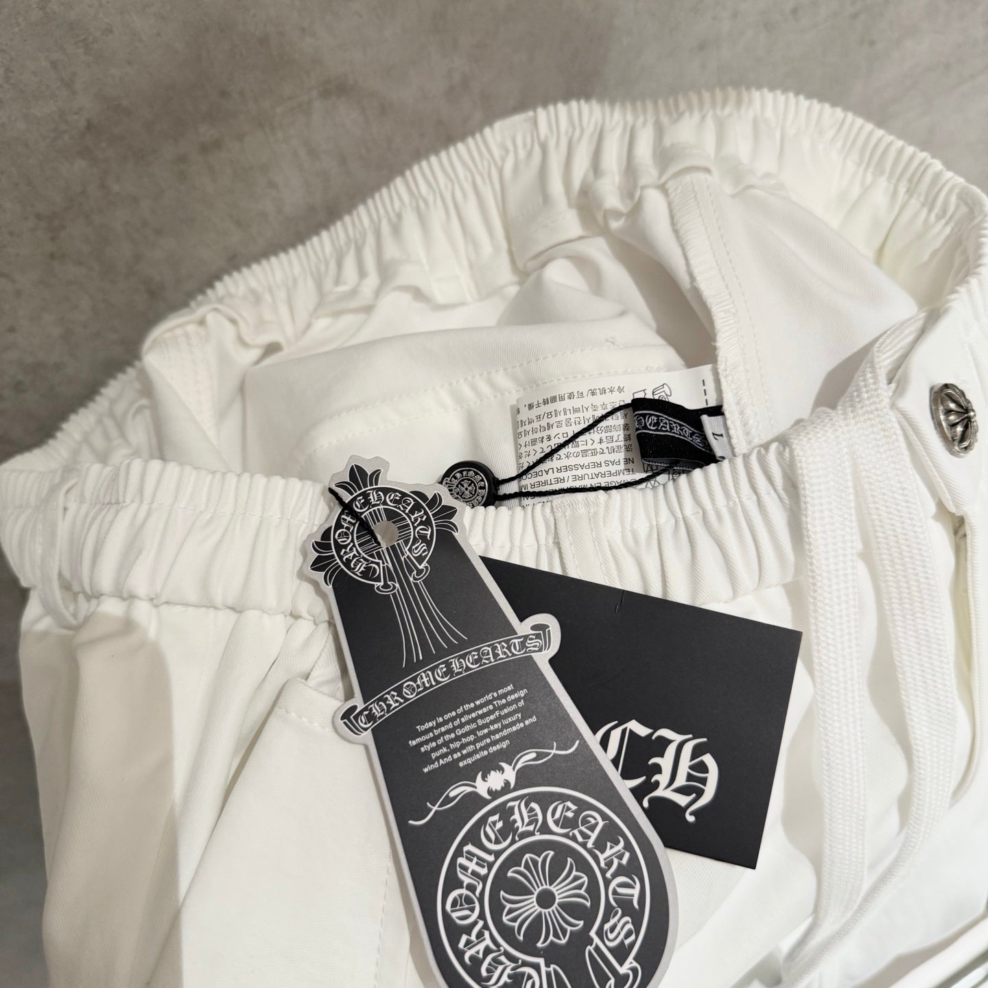 White pants waistband with hanging tags and silver-tone button