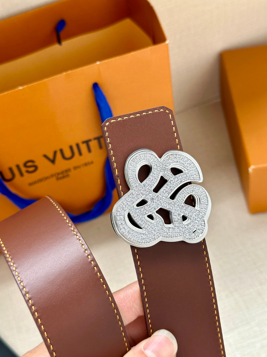 Brown leather belt with silver-tone logo buckle, close-up view