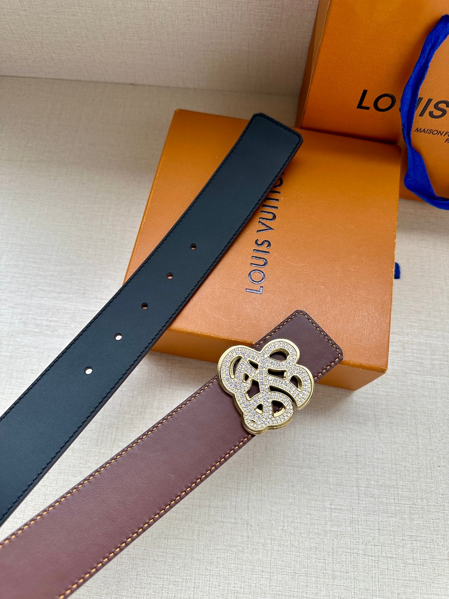 Brown leather belt with gold-tone logo buckle, close-up on strap